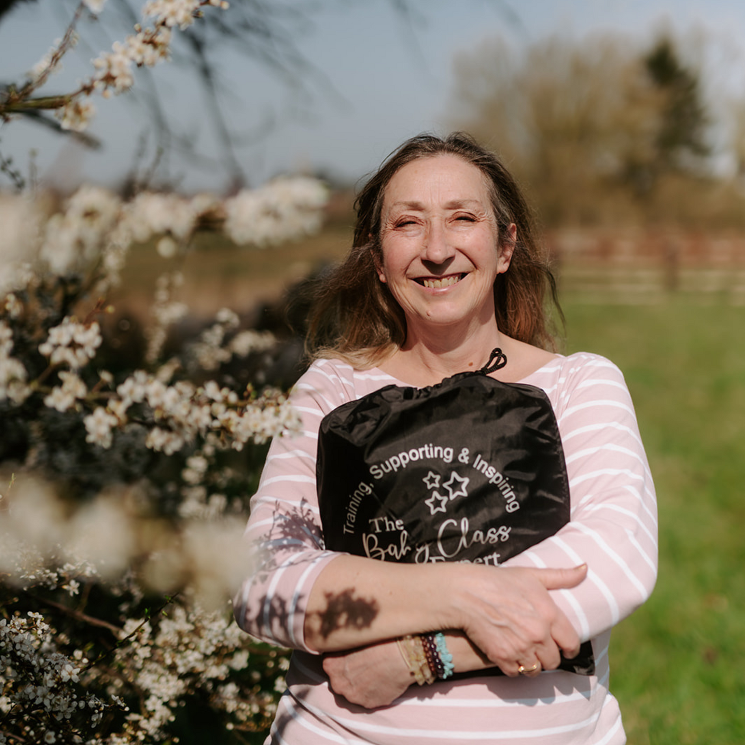 Elizabeth James, founder of The Baby Class Expert, holding a sensory parachute bag under a blossom tree