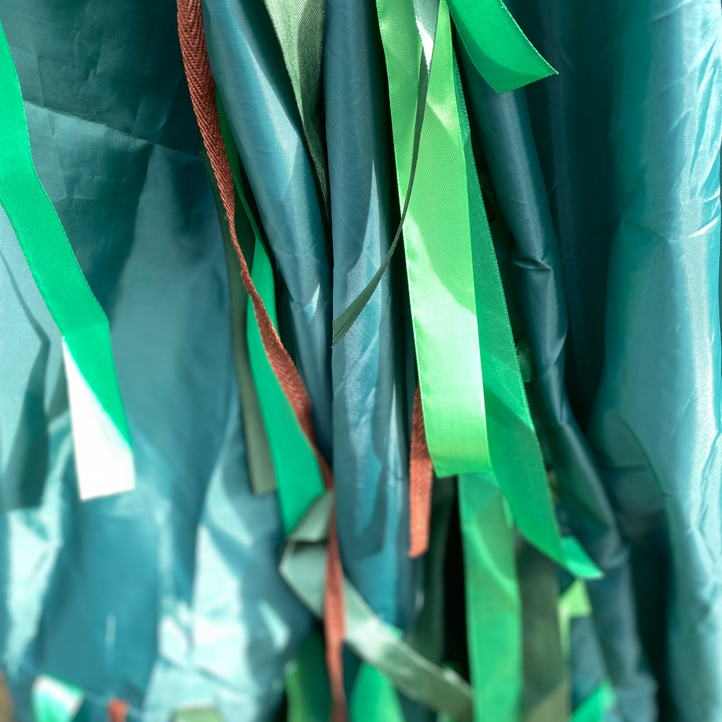 Varying shades of green ribbons and brown ribbon hanging down from the Jungle Green Sensory Parachute