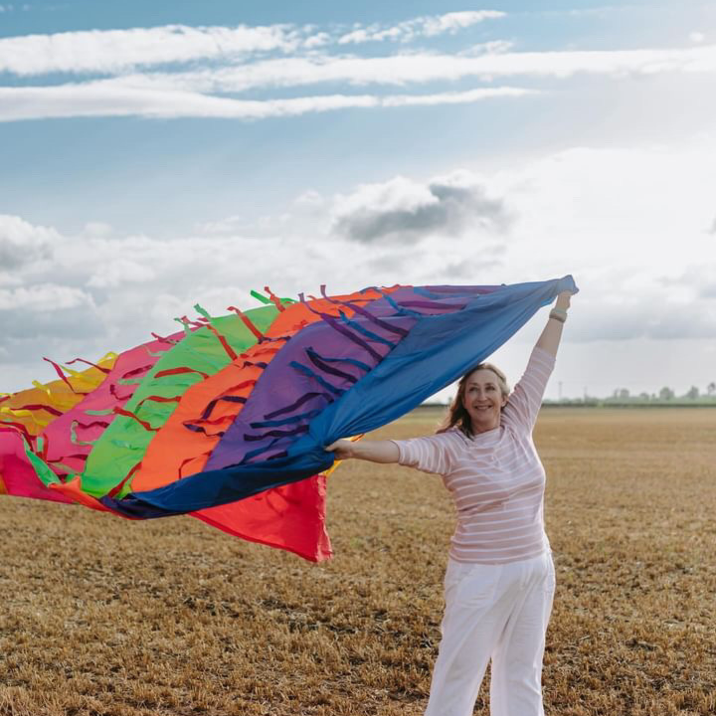 Rainbow sensory parachute held aloft outdoors, showing bright colours and flowing ribbons for baby development classes