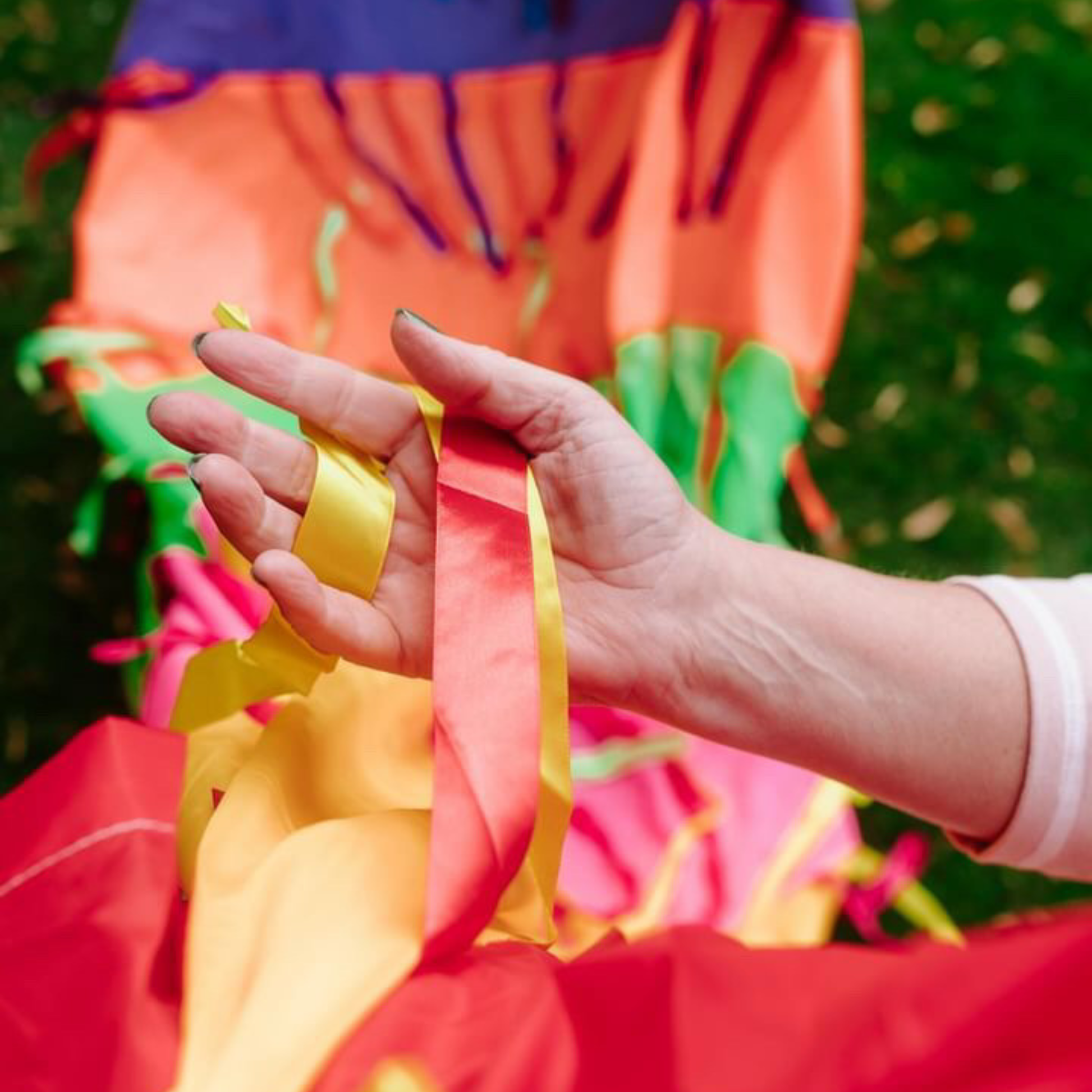 Hand holding satin ribbons from the rainbow sensory parachute used in baby classes and sensory play