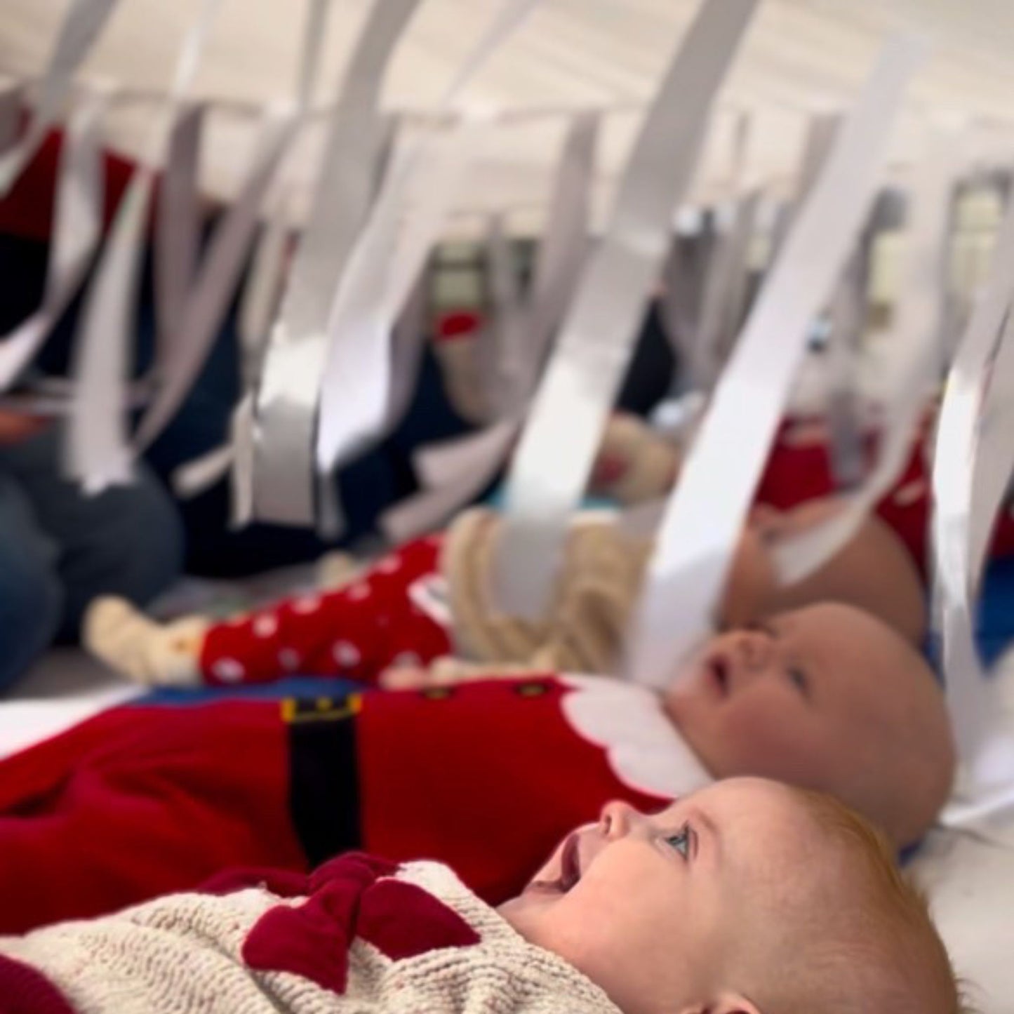 Babies lying beneath the Snowfall white sensory parachute during a baby development class, exploring light and movement