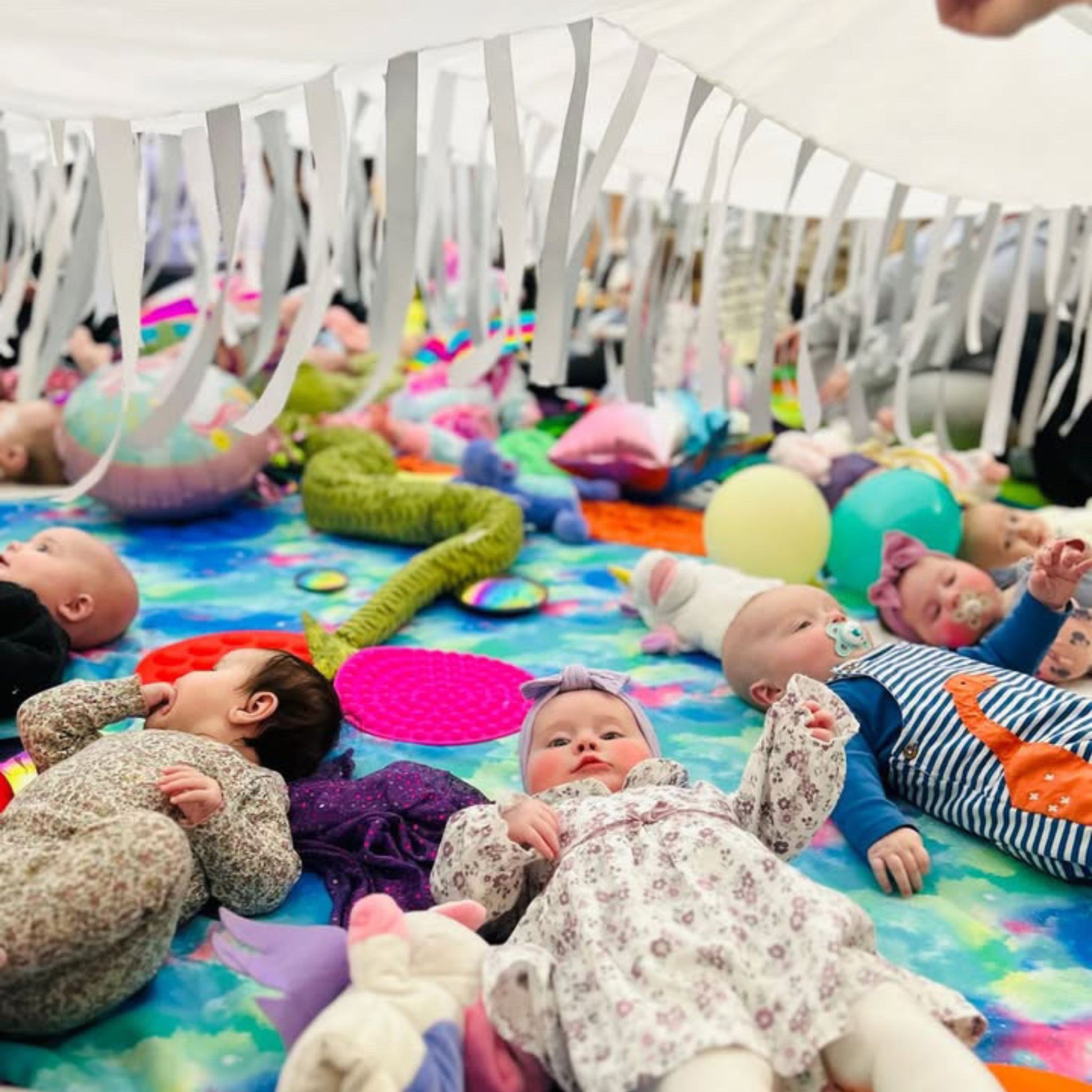 Babies enjoying sensory play beneath the Snowfall white parachute with ribbons and soft light in a baby class session